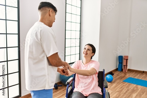 Young disabled woman and physiotherapist smiling happy shaking hands at the clinic.