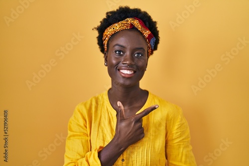 African young woman wearing african turban cheerful with a smile of face pointing with hand and finger up to the side with happy and natural expression on face