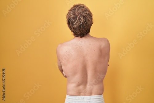 Caucasian man standing shirtless wearing sun screen standing backwards looking away with crossed arms