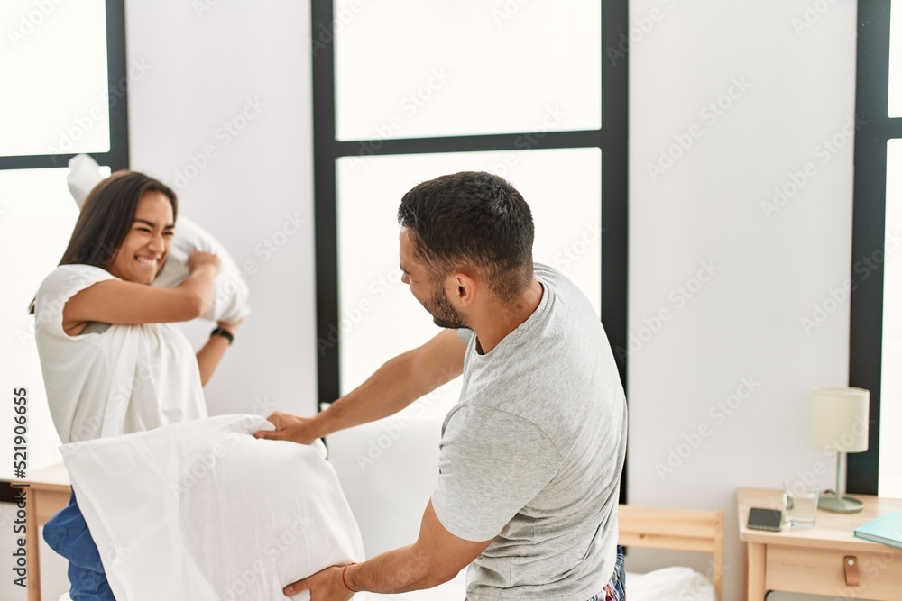 Fototapeta premium Young latin couple smiling happy fighting with pillows on the bed at home.