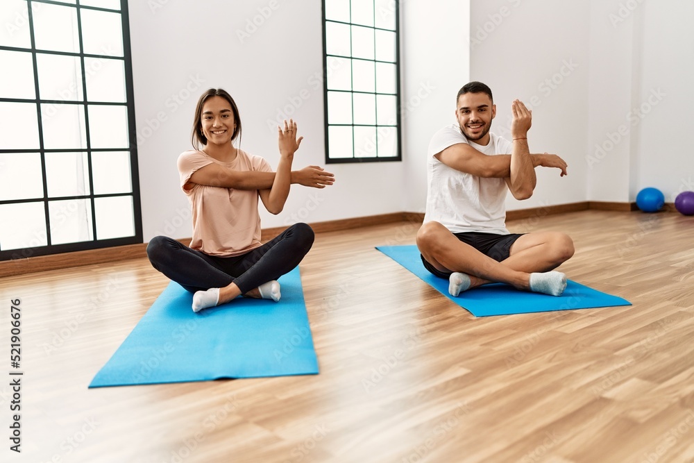 Fototapeta premium Latin man and woman couple smiling confident stretching at sport center
