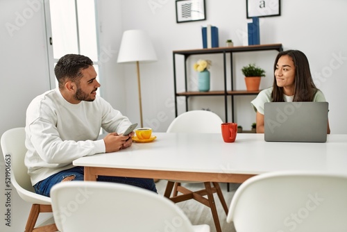 Young latin couple using laptop and smartphone drinking coffee at home.