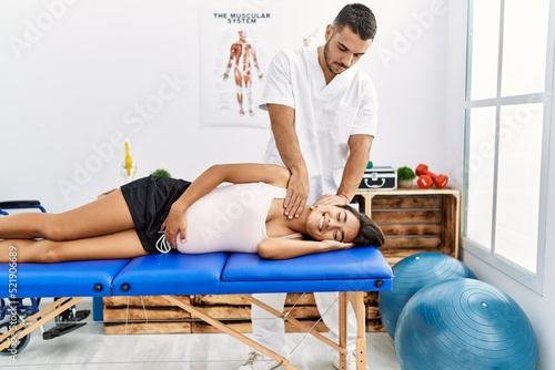 Latin man and woman wearing physiotherapist uniform having pregnancy rehab session stretching neck at physiotherapy clinic
