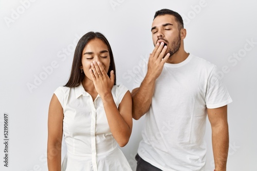 Young interracial couple standing together in love over isolated background bored yawning tired covering mouth with hand. restless and sleepiness.