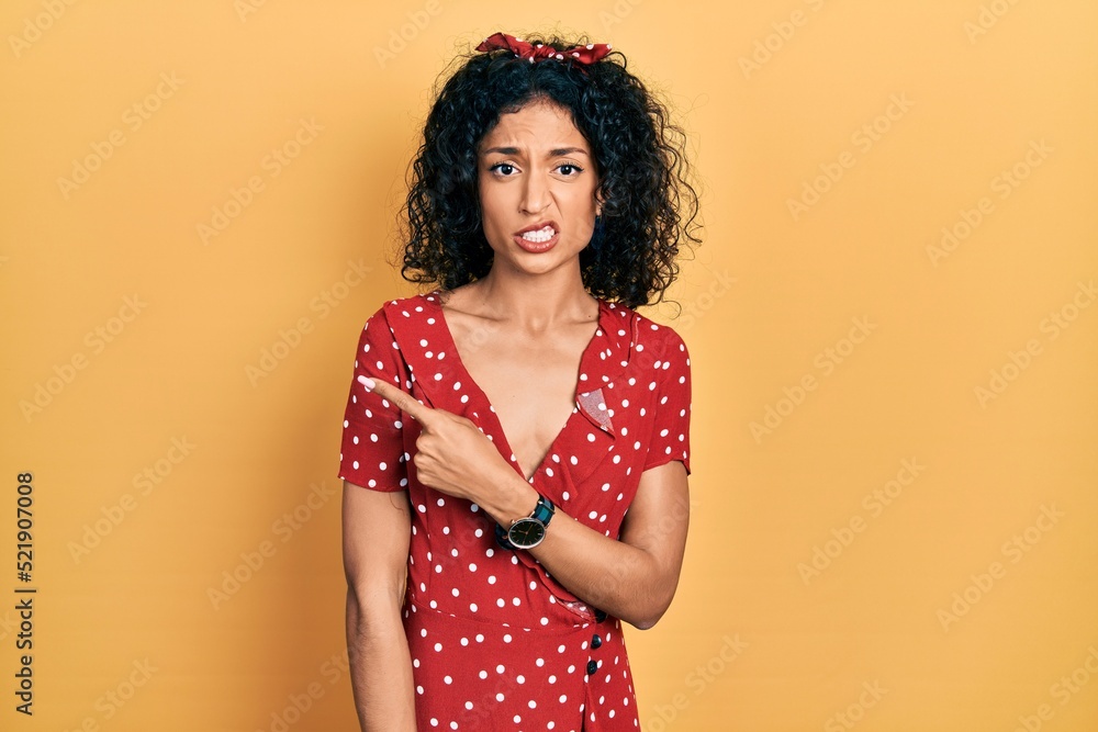 Young latin girl wearing summer dress pointing aside worried and nervous with forefinger, concerned and surprised expression Young latin girl wearing summer dress pointing aside worried and nervous with forefinger, concerned and surprised expression