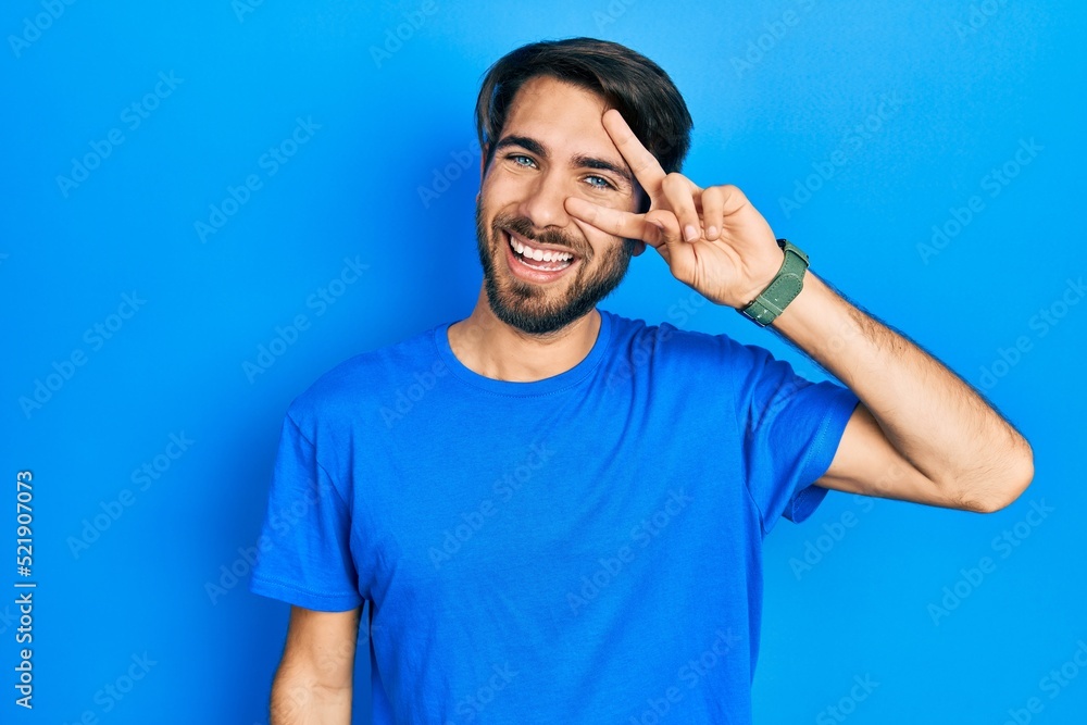 Young hispanic man wearing casual clothes doing peace symbol with fingers over face, smiling cheerful showing victory Young hispanic man wearing casual clothes doing peace symbol with fingers over face, smiling cheerful showing victory