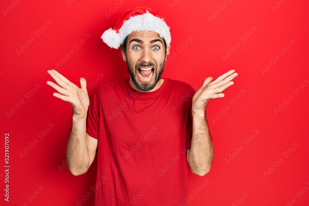 Young hispanic man wearing christmas hat celebrating crazy and amazed for success with arms raised and open eyes screaming excited. winner concept Young hispanic man wearing christmas hat celebrating crazy and amazed for success with arms raised and open eyes screaming excited. winner concept