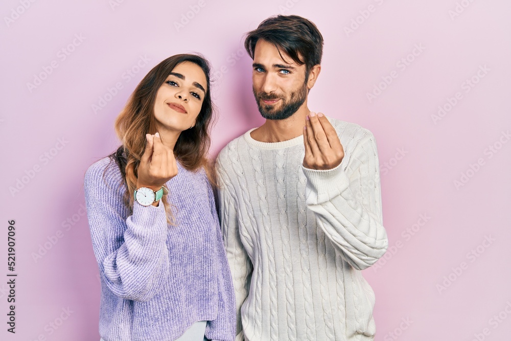 Fototapeta premium Young hispanic couple wearing casual clothes doing money gesture with hands, asking for salary payment, millionaire business