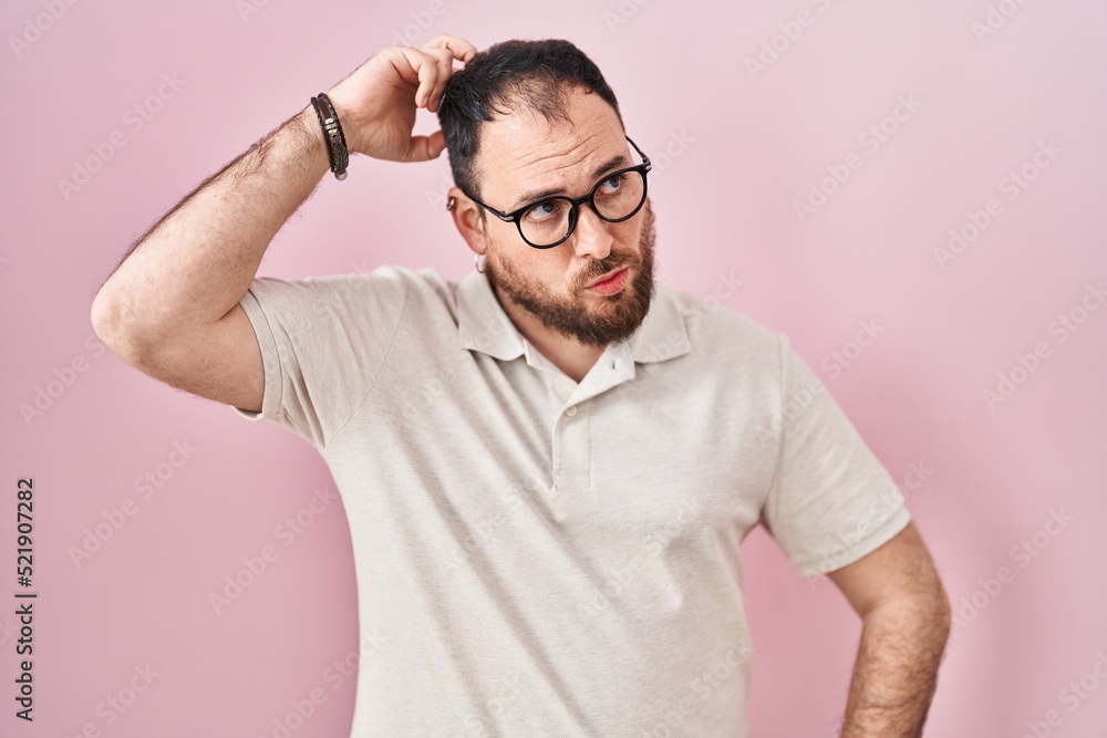 Fototapeta premium Plus size hispanic man with beard standing over pink background confuse and wondering about question. uncertain with doubt, thinking with hand on head. pensive concept.