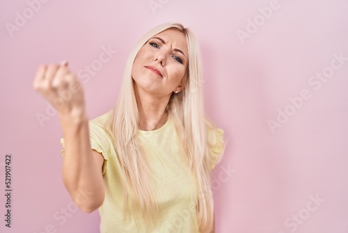 Caucasian woman standing over pink background angry and mad raising fist frustrated and furious while shouting with anger. rage and aggressive concept.