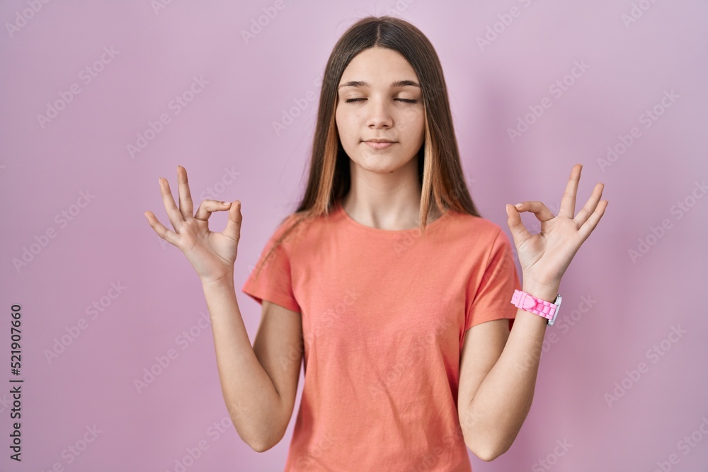 Teenager girl standing over pink background relaxed and smiling with eyes closed doing meditation gesture with fingers. yoga concept. Teenager girl standing over pink background relaxed and smiling with eyes closed doing meditation gesture with fingers. yoga concept.