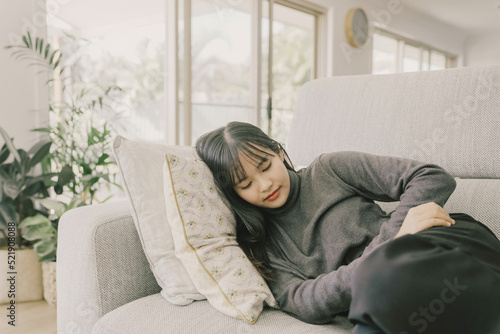 Young Asian woman lying down on sofa at home, stomach pain, gut health care concept