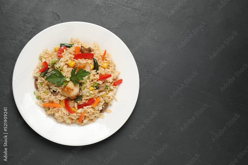Delicious rice pilaf with chicken and vegetables on black table, top view. Space for text Delicious rice pilaf with chicken and vegetables on black table, top view. Space for text