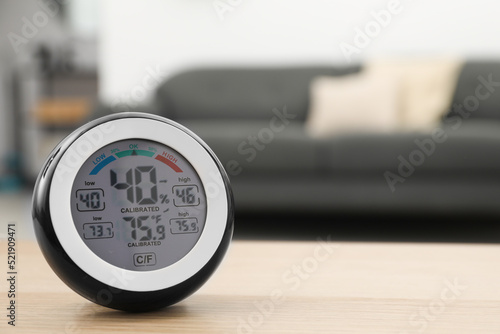 Digital hygrometer with thermometer on wooden table in room. Space for text photo