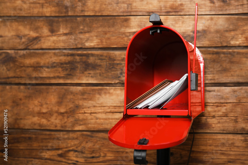 Open red letter box with envelopes against wooden background. Space for text photo