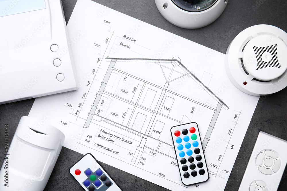 Fototapeta premium Building plan, remote controls, smoke and movement detectors on grey table, flat lay. Home security system