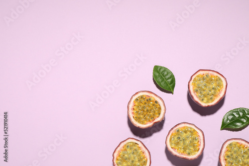 Halves of passion fruits (maracuyas) and green leaves on pink background, flat lay. Space for text