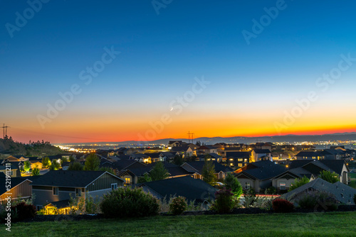 A crescent moon moves across the red late summer sunset sky over the lights of the cities of Spokane, Spokane Valley and Liberty Lake.