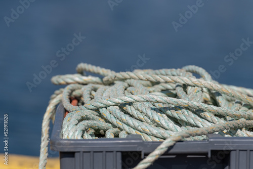 A tangled cluster of green and pink fishing rope pilled up on a wharf. The rope is worn and textured from being exposed to the weather. It looks dirty with grease or oil stains. The rope is braided.