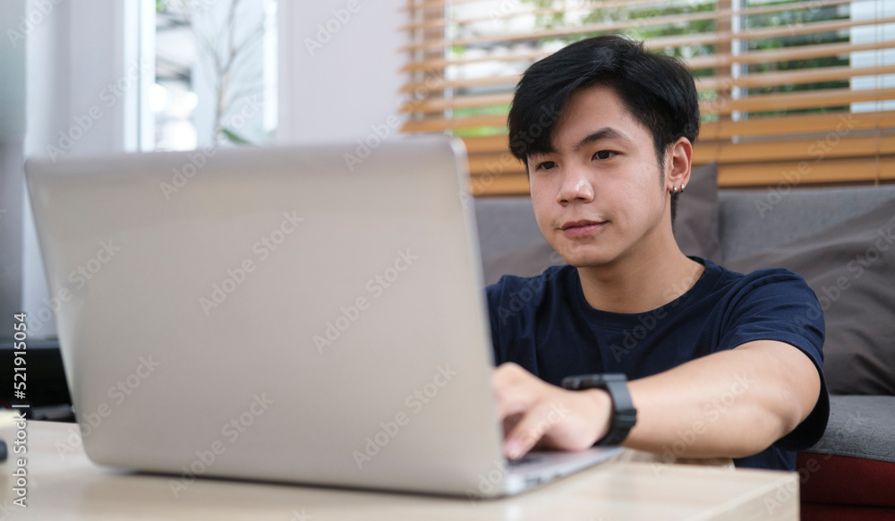 Smiling handsome asian man sitting on floor in living room and using laptop computer.. Smiling handsome asian man sitting on floor in living room and using laptop computer..