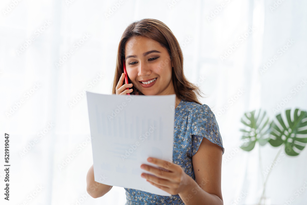 Young pretty Asian business woman talking on the phone when using laptop at working desk in modern office workplace. Young pretty Asian business woman talking on the phone when using laptop at working desk in modern office workplace.