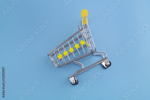 Rating, shopping and feedback concept. Shopping cart with five yellow stars on blue background.