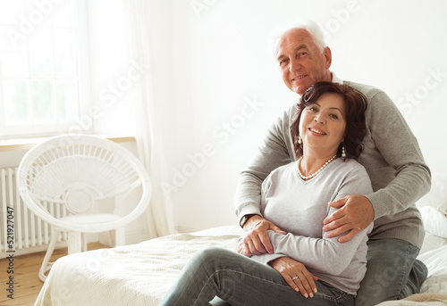 Mature 60 year old couple hugging while sitting on the bed in the bedroom. Love forever.