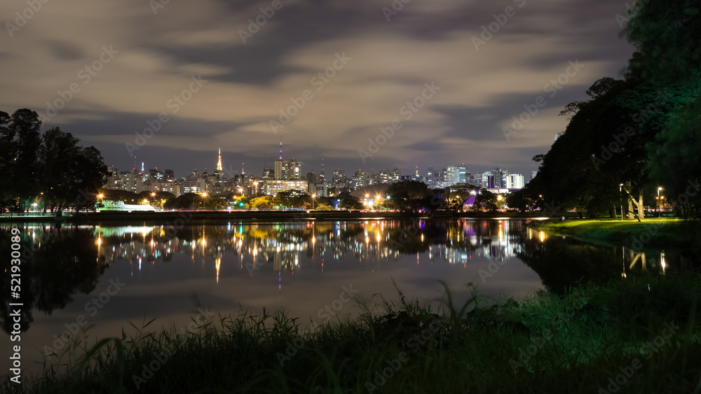 View of Ibirapuera Park, first metropolitan park in São Paulo, Brazil, and one of the most visited parks in South America at night. In the background part of the city’s skyline reflected in a lagoon