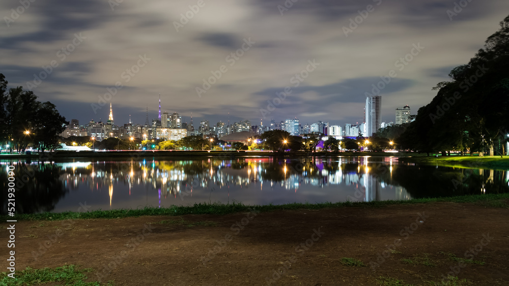 View of Ibirapuera Park, first metropolitan park in São Paulo, Brazil, and one of the most visited parks in South America at night. In the background part of the city’s skyline reflected in a lagoon