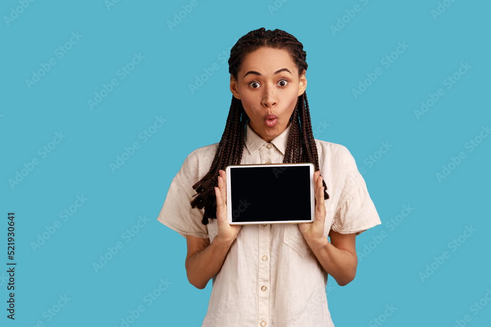 Astonished surprised woman holds modern tablet with empty display for your promotional text, poses with electronic device in hands, wearing white shirt. Indoor studio shot isolated on blue background. Astonished surprised woman holds modern tablet with empty display for your promotional text, poses with electronic device in hands, wearing white shirt. Indoor studio shot isolated on blue background.