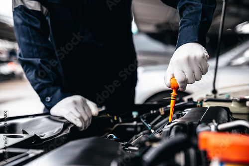 Mechanic inspecting oil level in a engine at garage workshop, Car auto services and maintenance check concept.