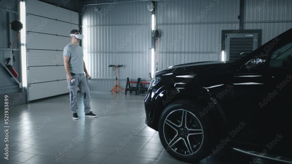 In car service mechanic in uniform checking and diagnosing a car with a breakdown after a crash using modern virtual reality glasses with controllers In car service mechanic in uniform checking and diagnosing a car with a breakdown after a crash using modern virtual reality glasses with controllers