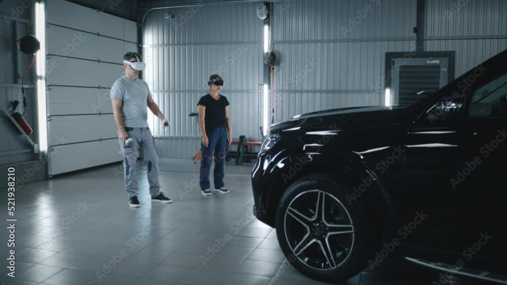 Diverse car service workers in uniform checking and inspecting a car together during diagnostics wearing virtual reality headsets with controllers Diverse car service workers in uniform checking and inspecting a car together during diagnostics wearing virtual reality headsets with controllers