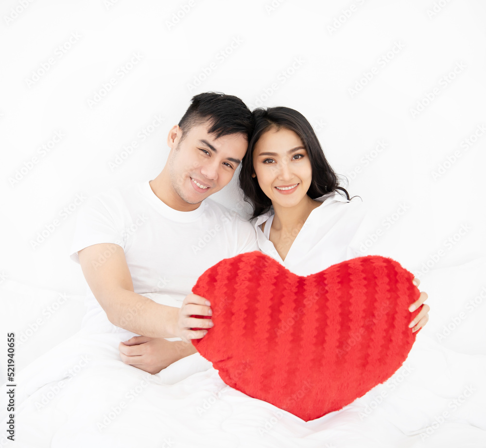 smiling couple in bed with red heart-shaped pillow.in , holidays and happiness concept