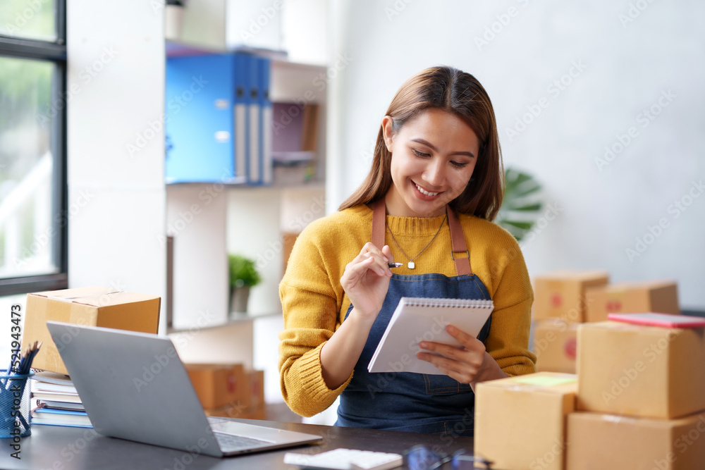 Happy young Asian business owner woman prepare parcel box and check online orders of product for deliver to customer on laptop computer. Shopping Online concept. Happy young Asian business owner woman prepare parcel box and check online orders of product for deliver to customer on laptop computer. Shopping Online concept.
