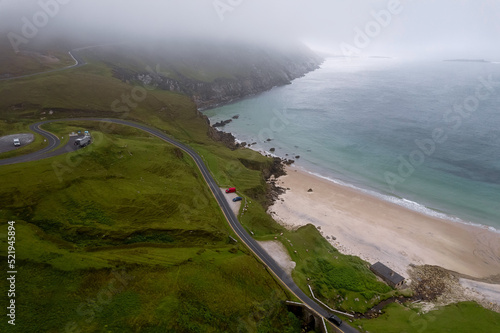 Small road and bridge by a stunning Keem beach and Atlantic ocean. Ireland. Popular travel area with water sports and stunning nature scenery. Aerial image. Cool morning time. Nobody.