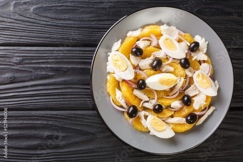 Remojon is a traditional Spanish salad made with a combination of oranges, salt cod, eggs, olive oil, olives, and wine vinegar close-up in a plate on the table. Horizontal top view from above