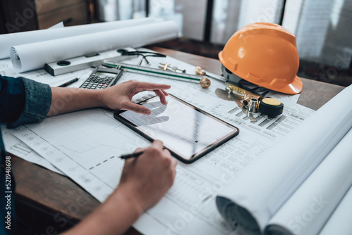 Engineering working with drawings inspection on tablet in the office and Calculator, triangle ruler, safety glasses, compass on Blueprint. Engineer, Architect, Industry and factory concept.