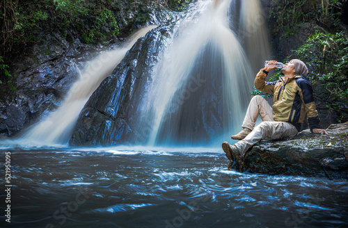Tourist man with backpack sit and drink water for relax at the waterfall
