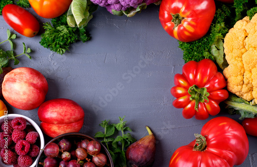 Mockup with harvest variation with assorted fruits and vegetables framing copy space on gray table. Tomatoes, cauliflower, peach, fig, raspberry and gooseberry in seasonal food composition