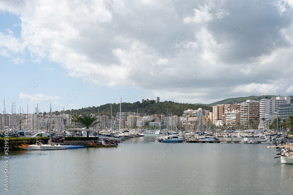 Urbanscape of the marina in Palma de Mallorca, Spain. There are clouds and a castle on the mountain