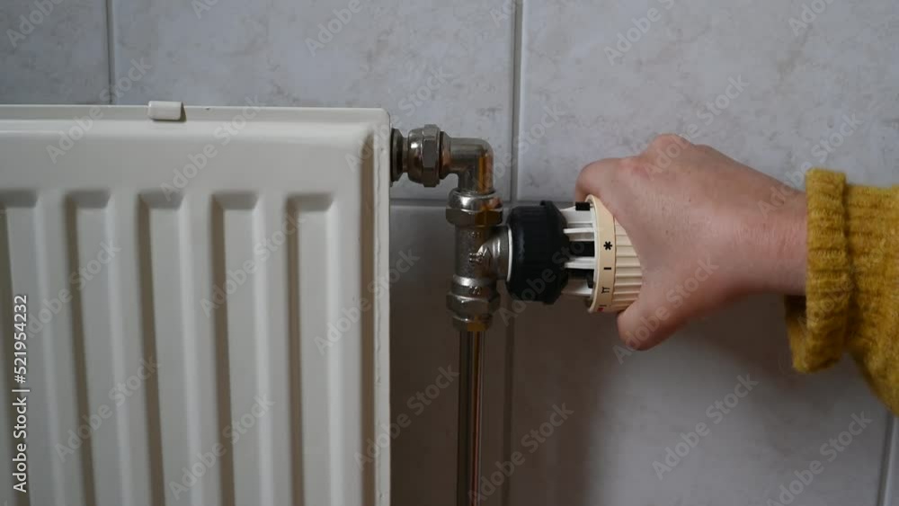 Person in a warm yellow sweater is turning on the heater at home. Closeup of hand turning up the thermostat on the radiator. Concept of energy and electricity consumption. Person in a warm yellow sweater is turning on the heater at home. Closeup of hand turning up the thermostat on the radiator. Concept of energy and electricity consumption.
