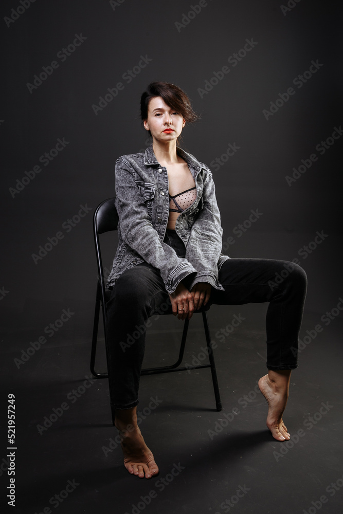 beautiful brunette girl in a jacket and jeans posing on a chair in the studio beautiful brunette girl in a jacket and jeans posing on a chair in the studio