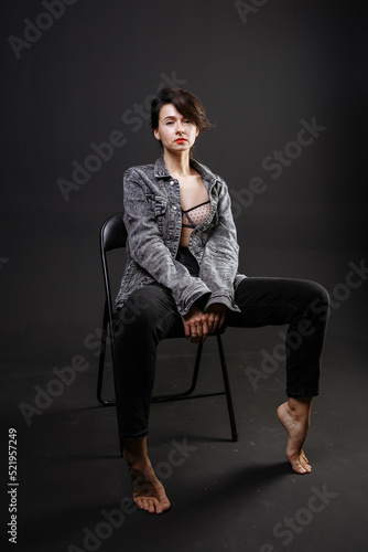 beautiful brunette girl in a jacket and jeans posing on a chair in the studio