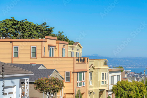 Three-storey suburban houses in a row with roof decks and a view of the bay in San Francisco, CA © Jason