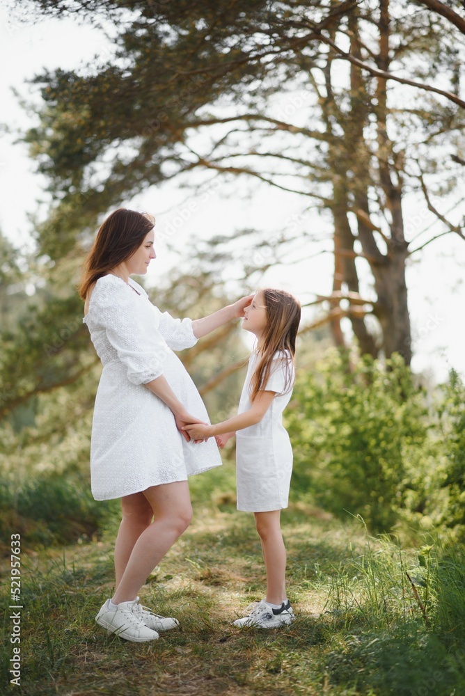 Fototapeta premium Pregnant woman and her daughter in the park at sunset. A happy family.
