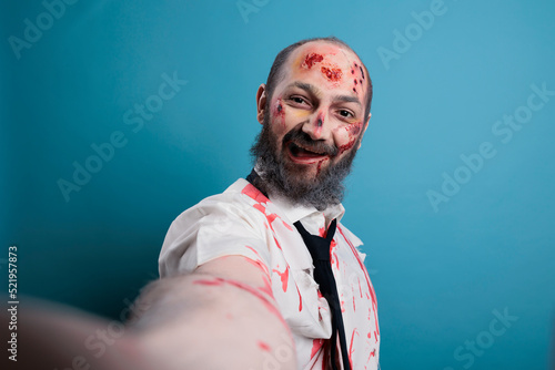 Halloween evil zombie taking photo on camera, posing in studio and looking dangerous. Brain eating corpse with bloody scars and wounds, horror aggressive monster with apocalyptic look.