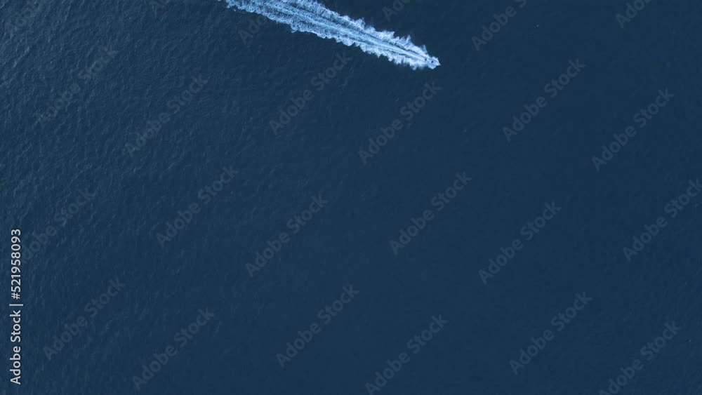 High aerial view of a speed boat cruising across the deep blue waters of the ocean. High aerial view of a speed boat cruising across the deep blue waters of the ocean.