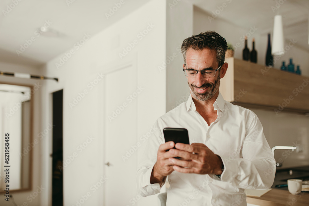 Smiling businessman using smart phone in kitchen at home Smiling businessman using smart phone in kitchen at home