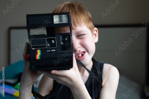 Child red-haired boy holds an old retro camera in his hands and makes a photo with a smile, children's hobby photography, life style portrait at home